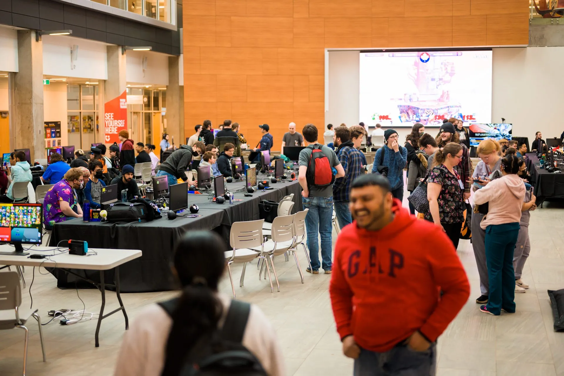 Rows of tournament stations and a match on the big screen at a Canakrn event